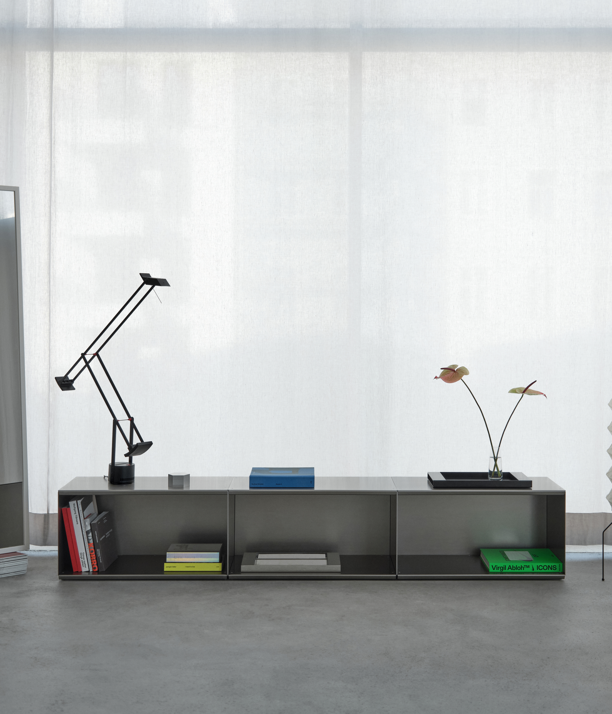 Modern M85 aluminum console made with modular elements with decorative items on a concrete floor in against a white curtain.