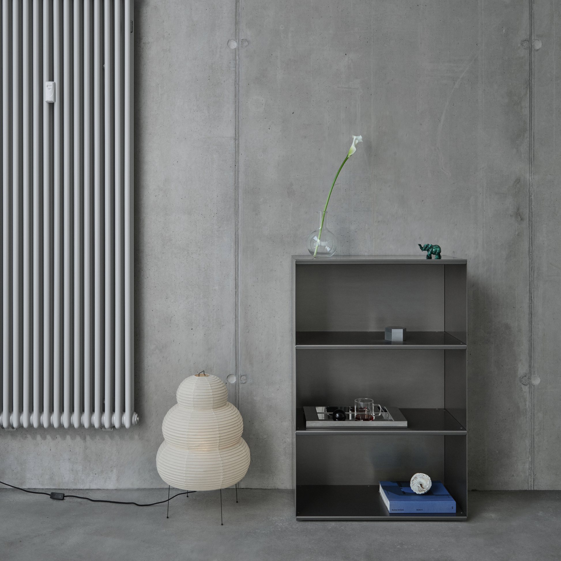 Modern interior with a radiator, M85 modular aluminum shelf, and decorative items against a concrete wall.
