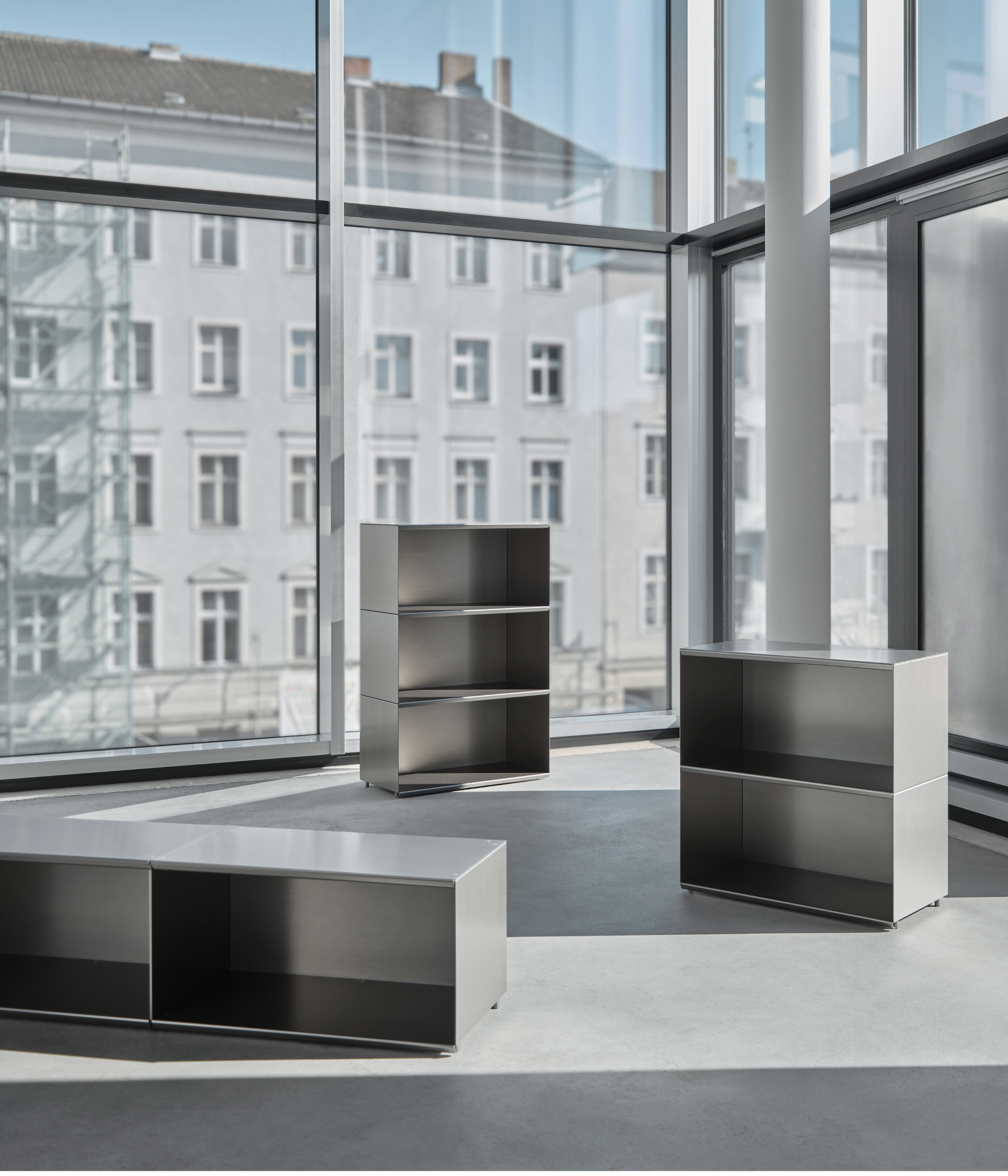 M85 Modern gunmetal aluminum modular furniture with bookshelves in front of large windows.