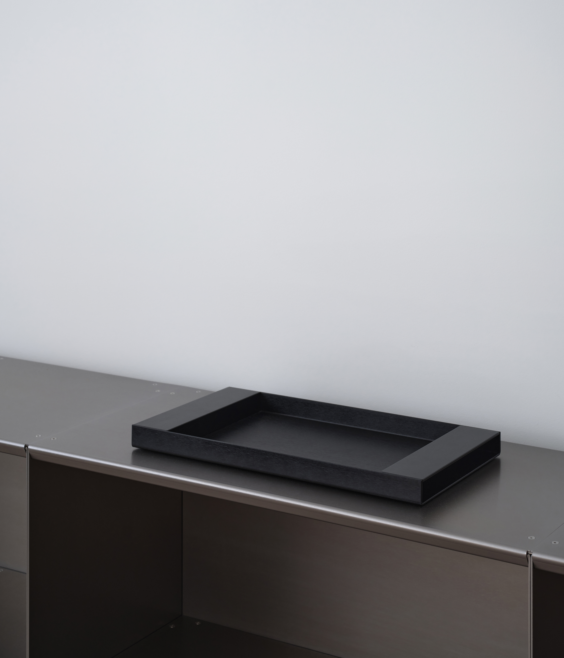 Perspective of black M85 aluminum tray on M85 modular bookshelf with a light gray background