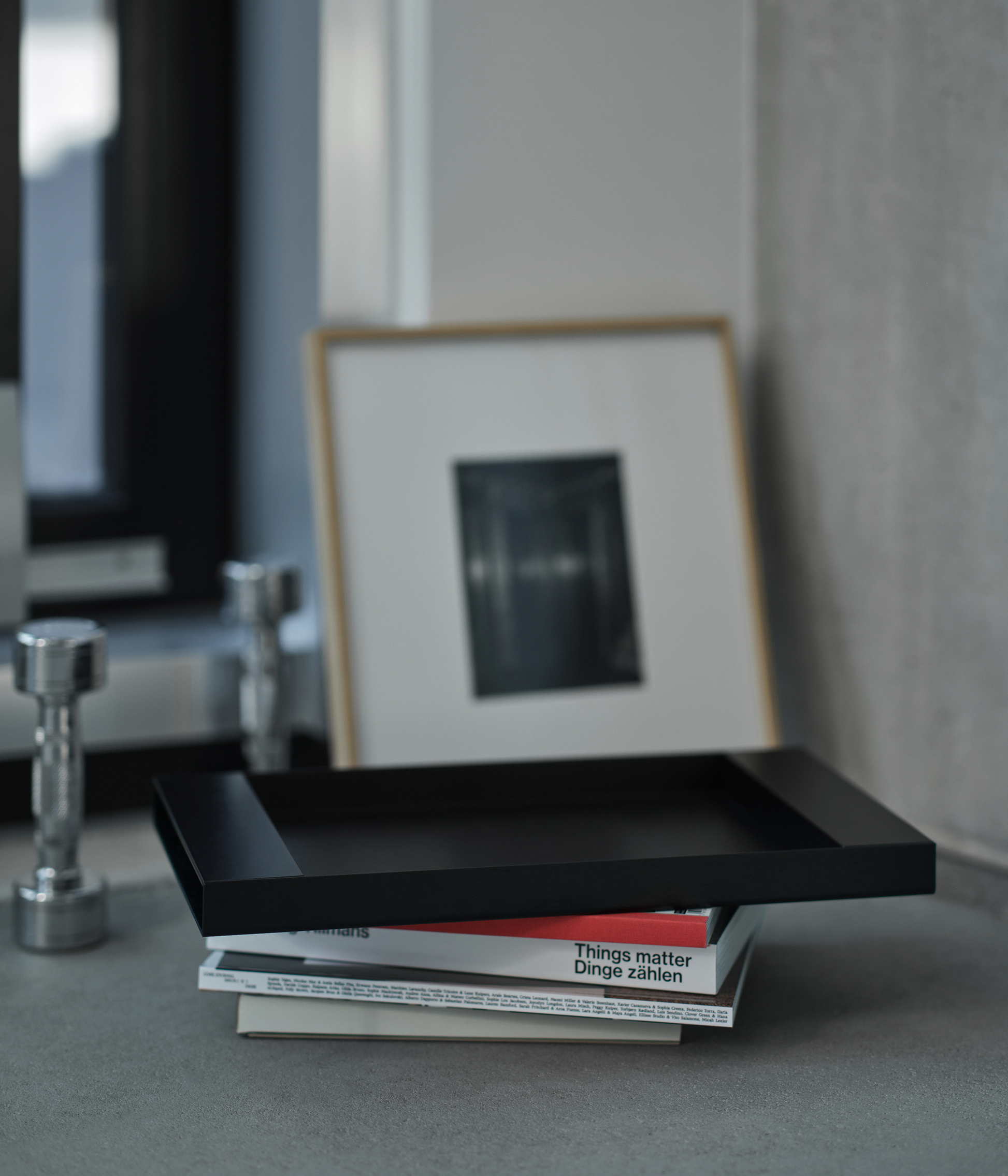 Black M85 tray with books and a framed picture on a gray surface