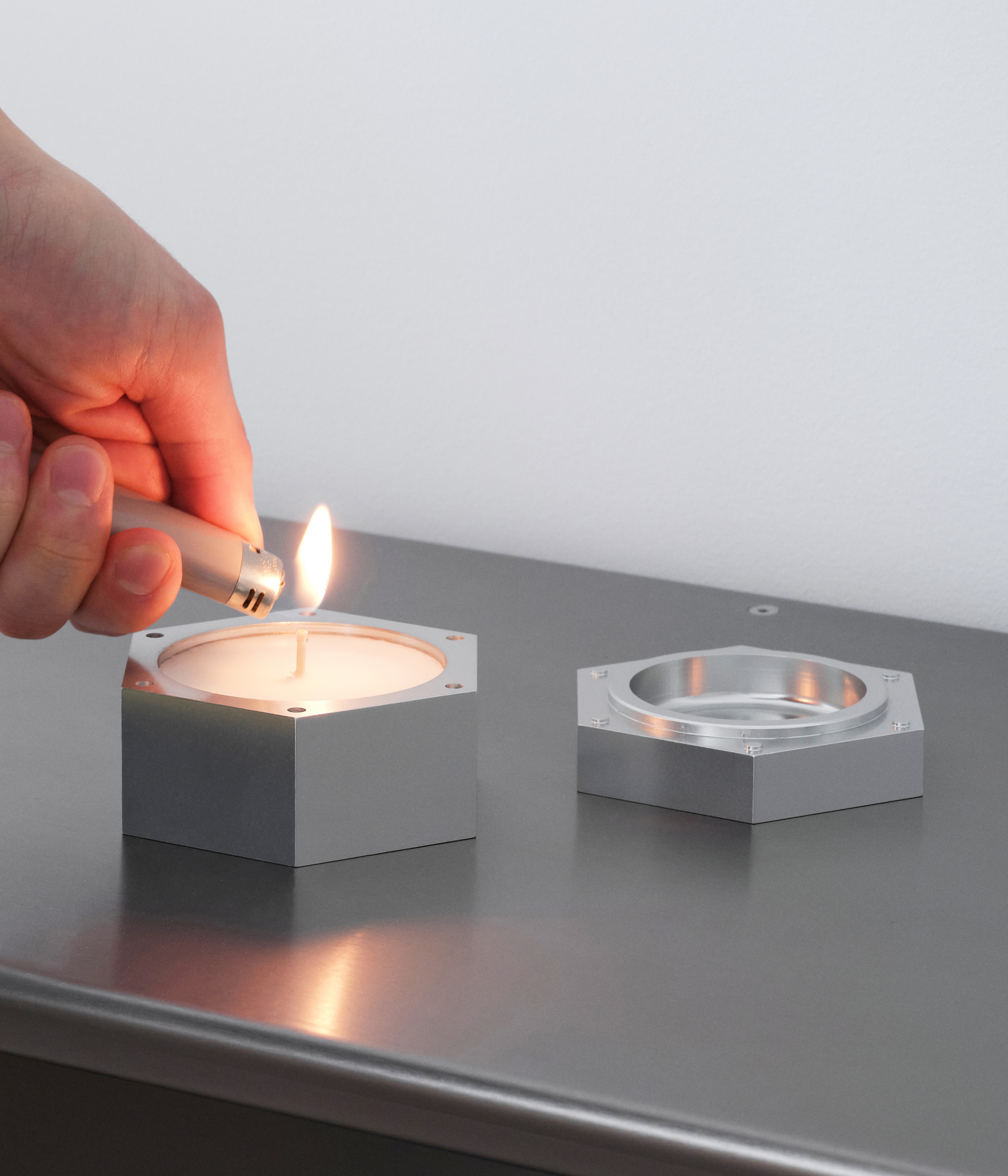 Hand lighting M85 aluminum and soy wax candle standing on M85 modular shelving system.