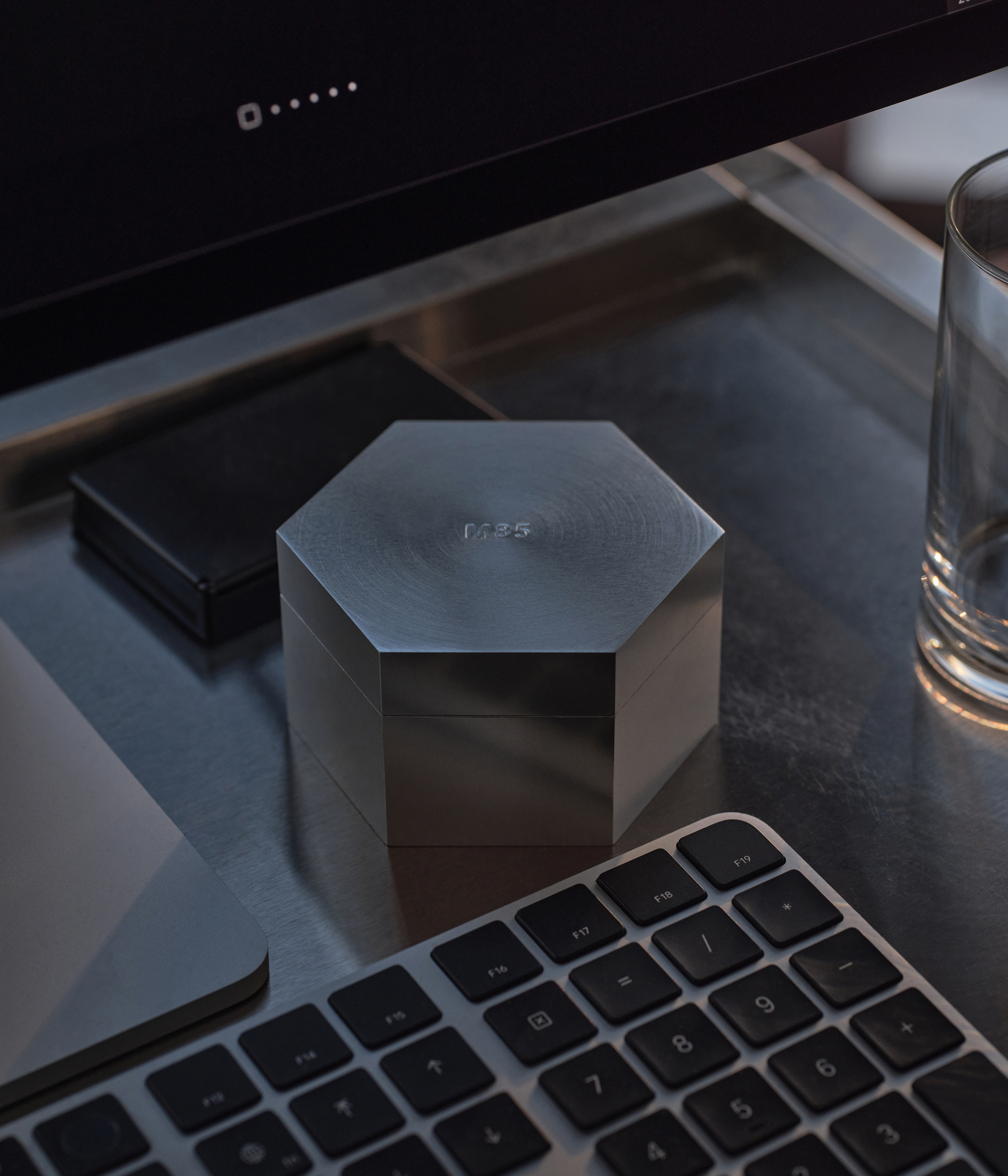 Aluminum hexagonal M85 candle on a desk with a computer monitor and keyboard in the background