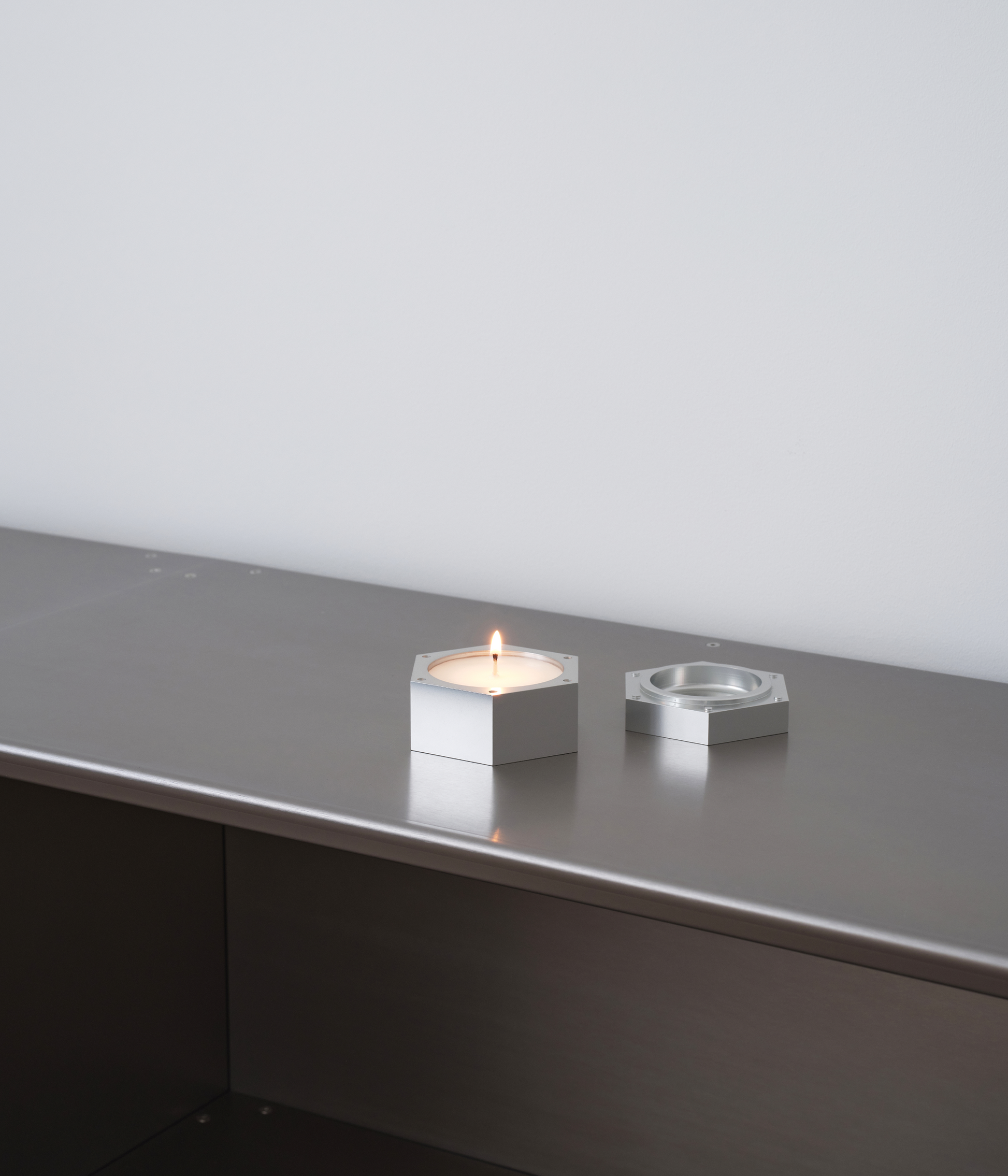 M85 aluminum hexagonal candle lit up standing on M85 bookshelf