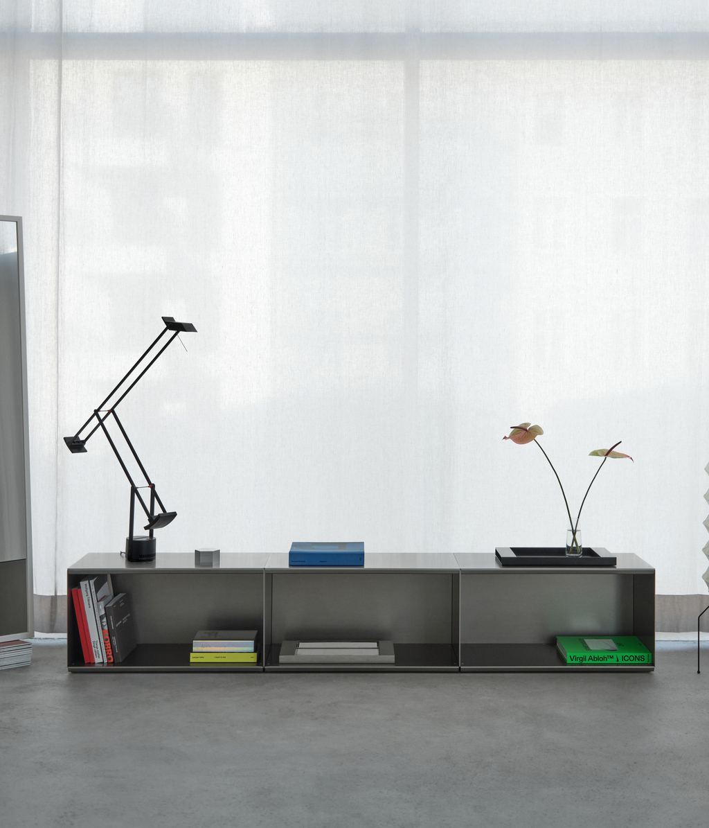 Modern M85 aluminum console made with modular elements with decorative items on a concrete floor in against a white curtain.