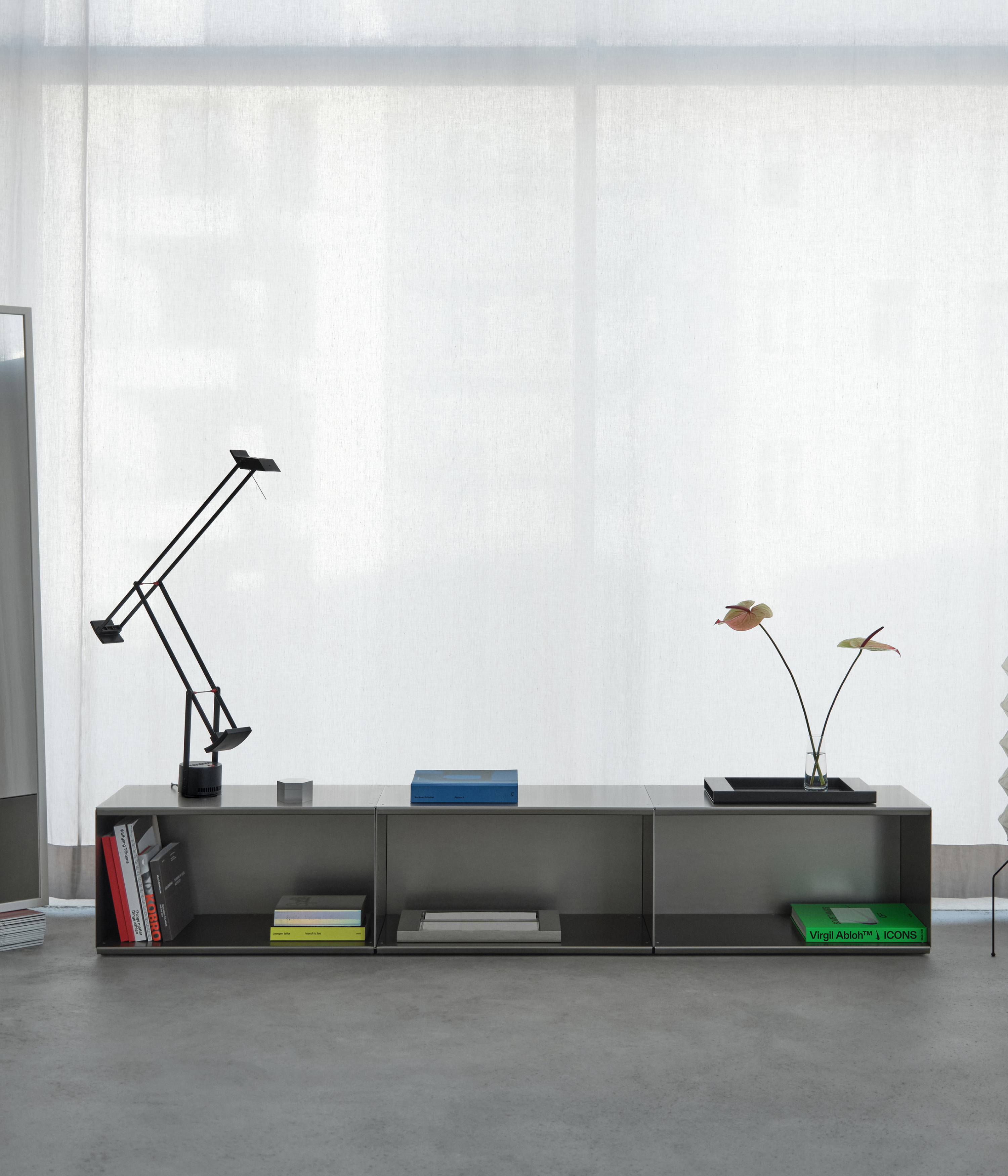 Modern M85 aluminum console made with modular elements with decorative items on a concrete floor in against a white curtain.