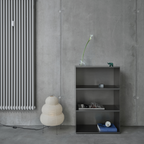 Modern interior with a radiator, M85 modular aluminum shelf, and decorative items against a concrete wall.