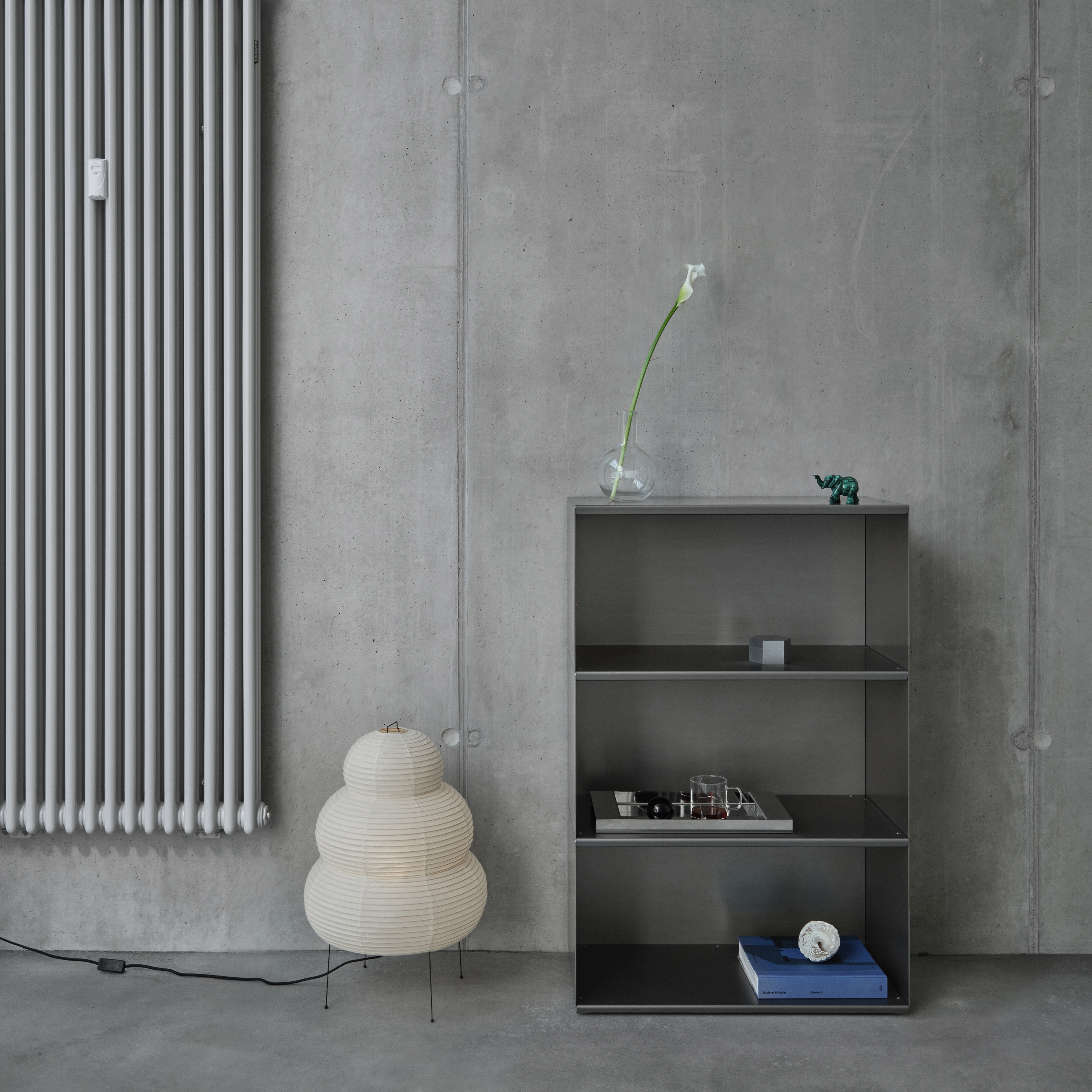 Modern interior with a radiator, M85 modular aluminum shelf, and decorative items against a concrete wall.