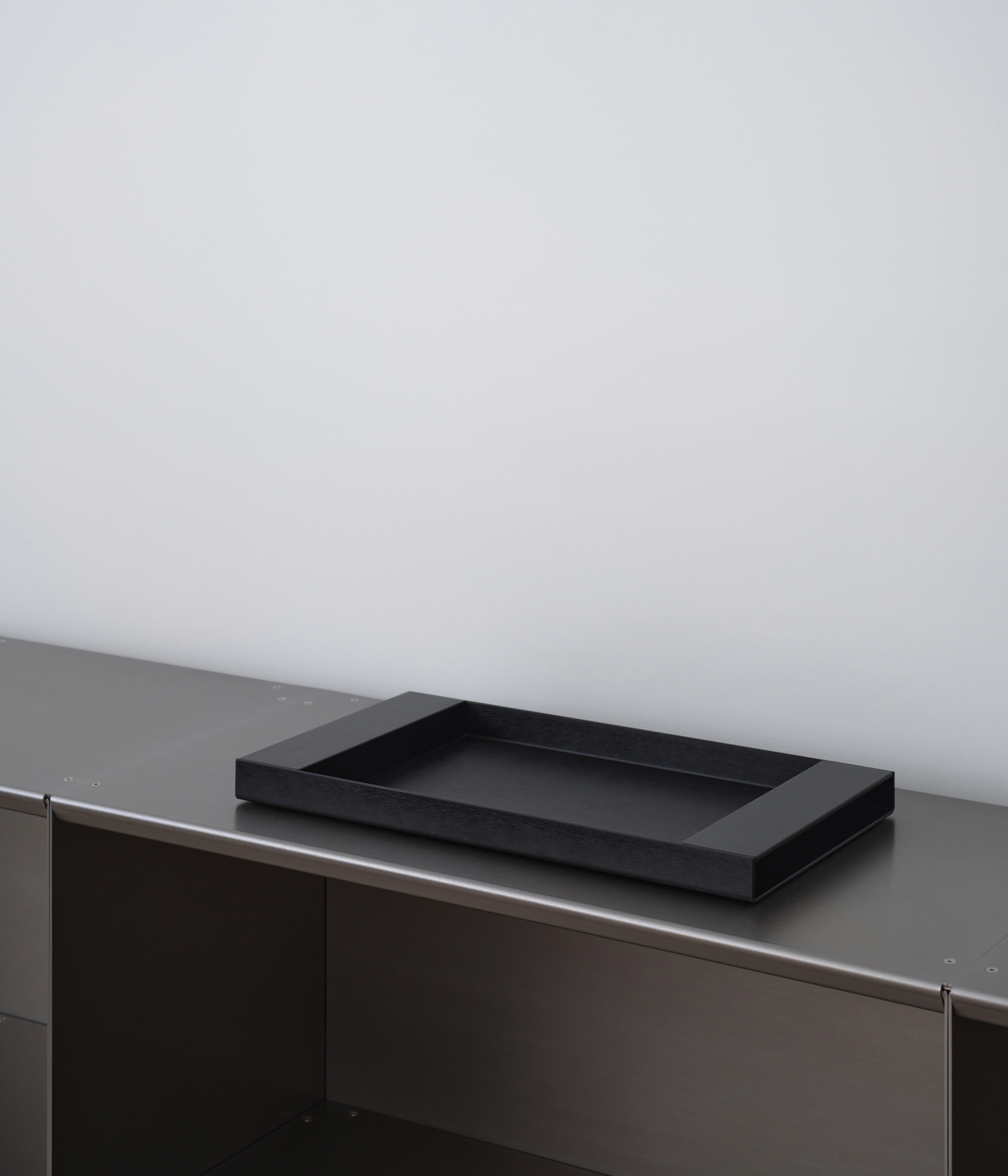 Perspective of black M85 aluminum tray on M85 modular bookshelf with a light gray background