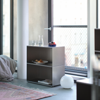 M85 modular aluminum side table with a glass of water and a plate of food in a living room with large windows.