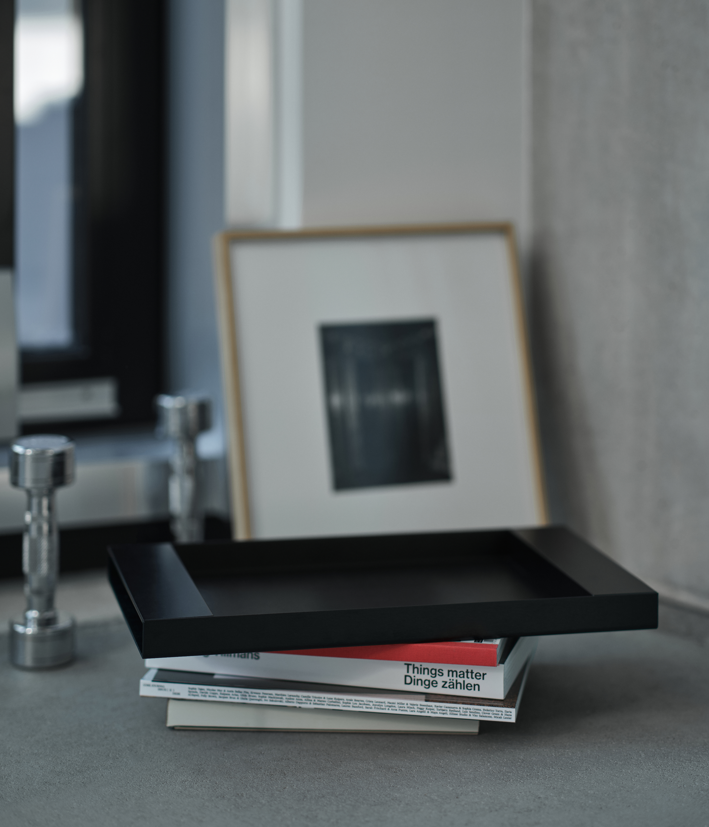 Black M85 tray with books and a framed picture on a gray surface