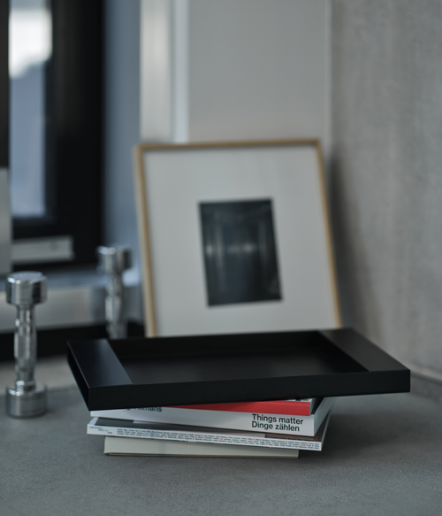 Black M85 tray with books and a framed picture on a gray surface