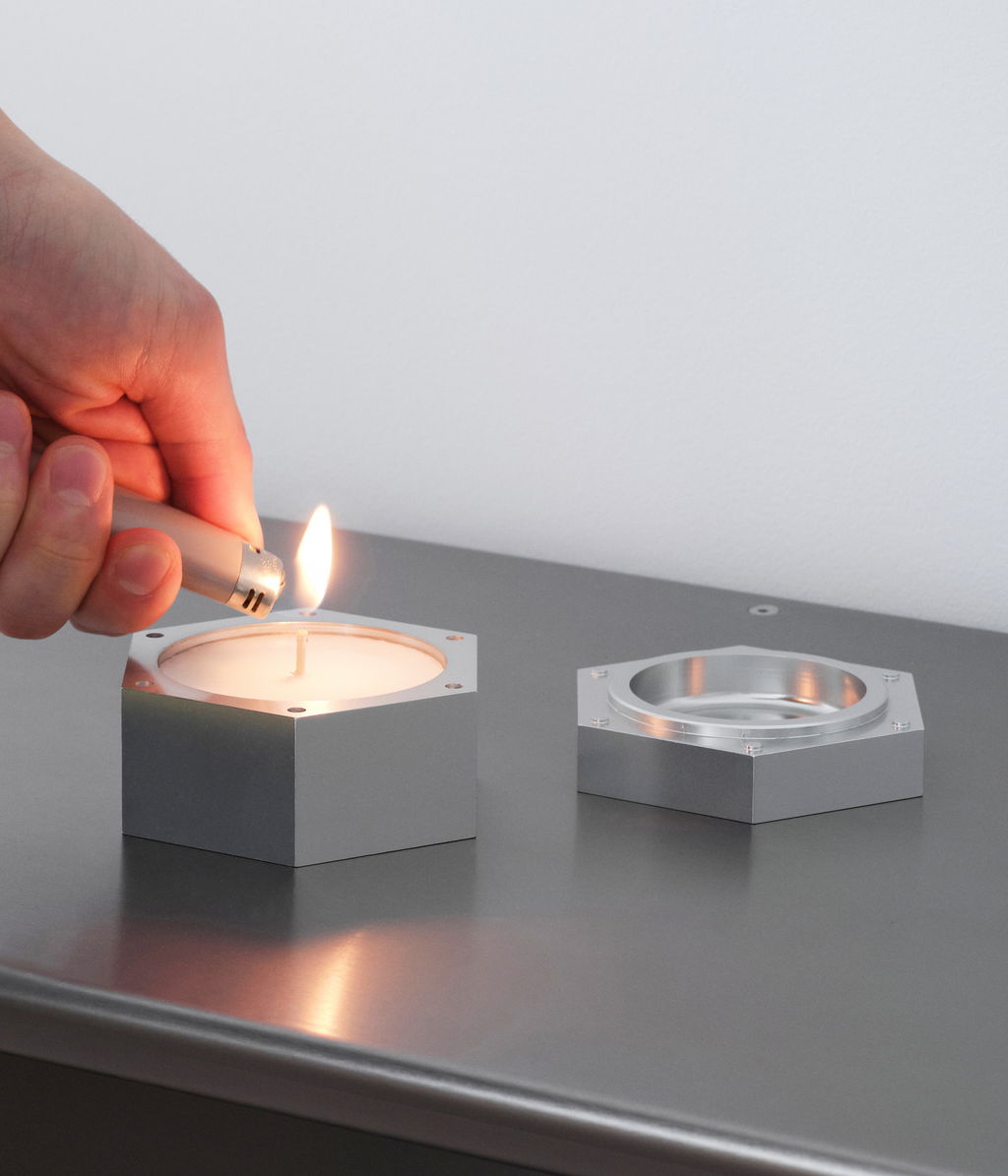 Hand lighting M85 aluminum and soy wax candle standing on M85 modular shelving system.