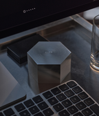 Aluminum hexagonal M85 candle on a desk with a computer monitor and keyboard in the background