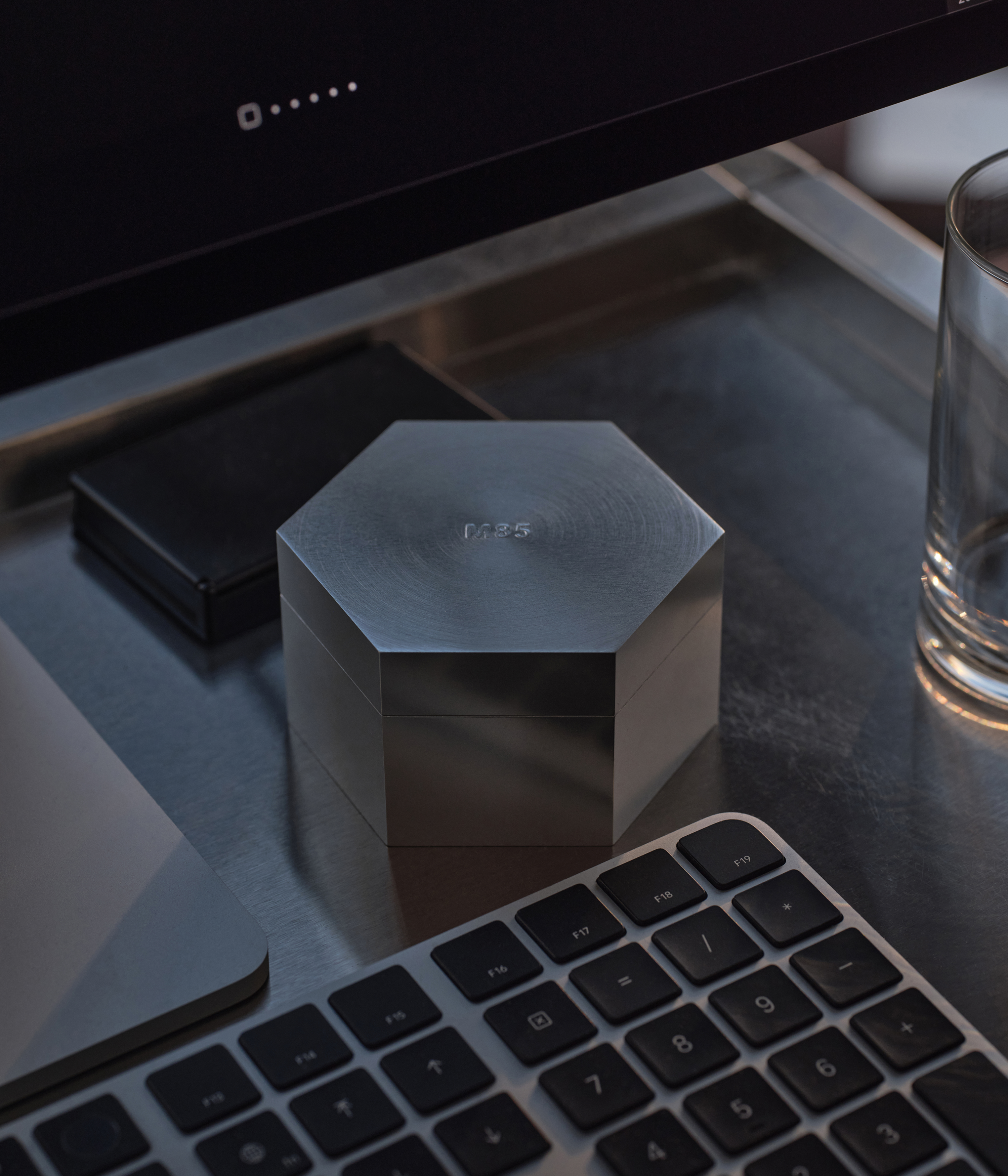Aluminum hexagonal M85 candle on a desk with a computer monitor and keyboard in the background