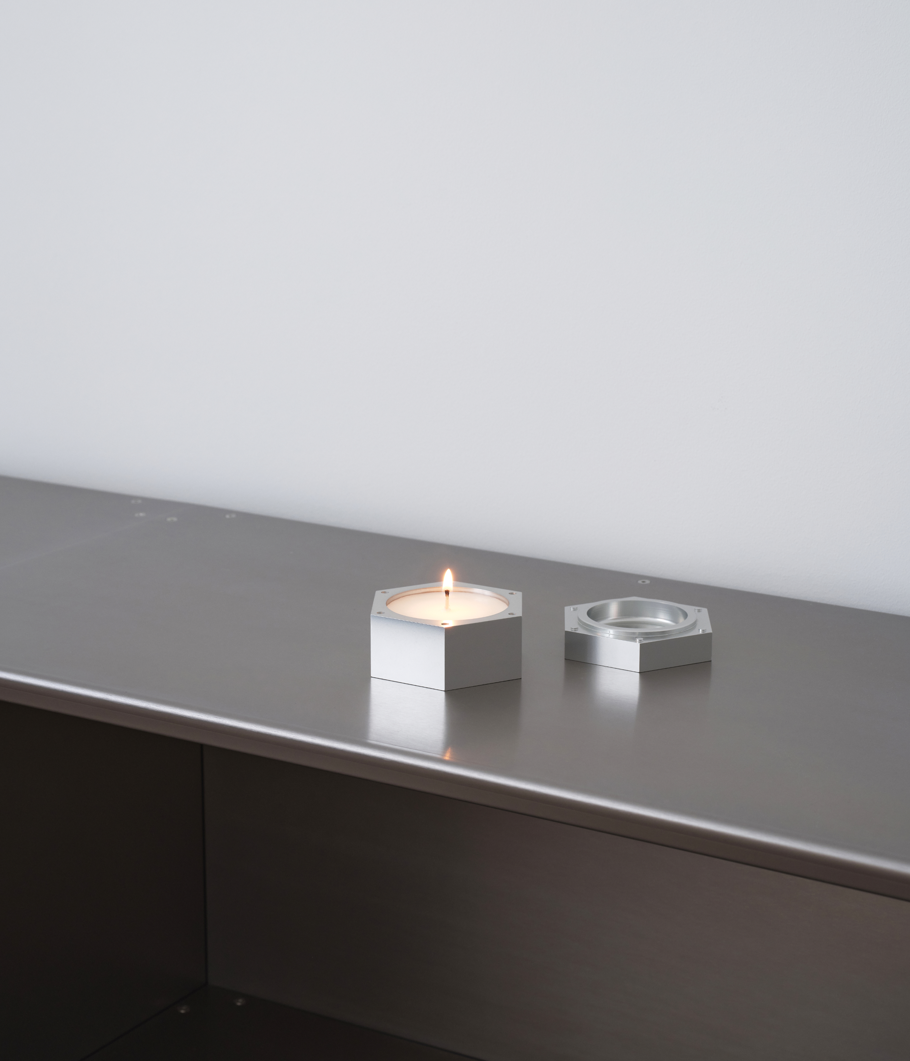 M85 aluminum hexagonal candle lit up standing on M85 bookshelf